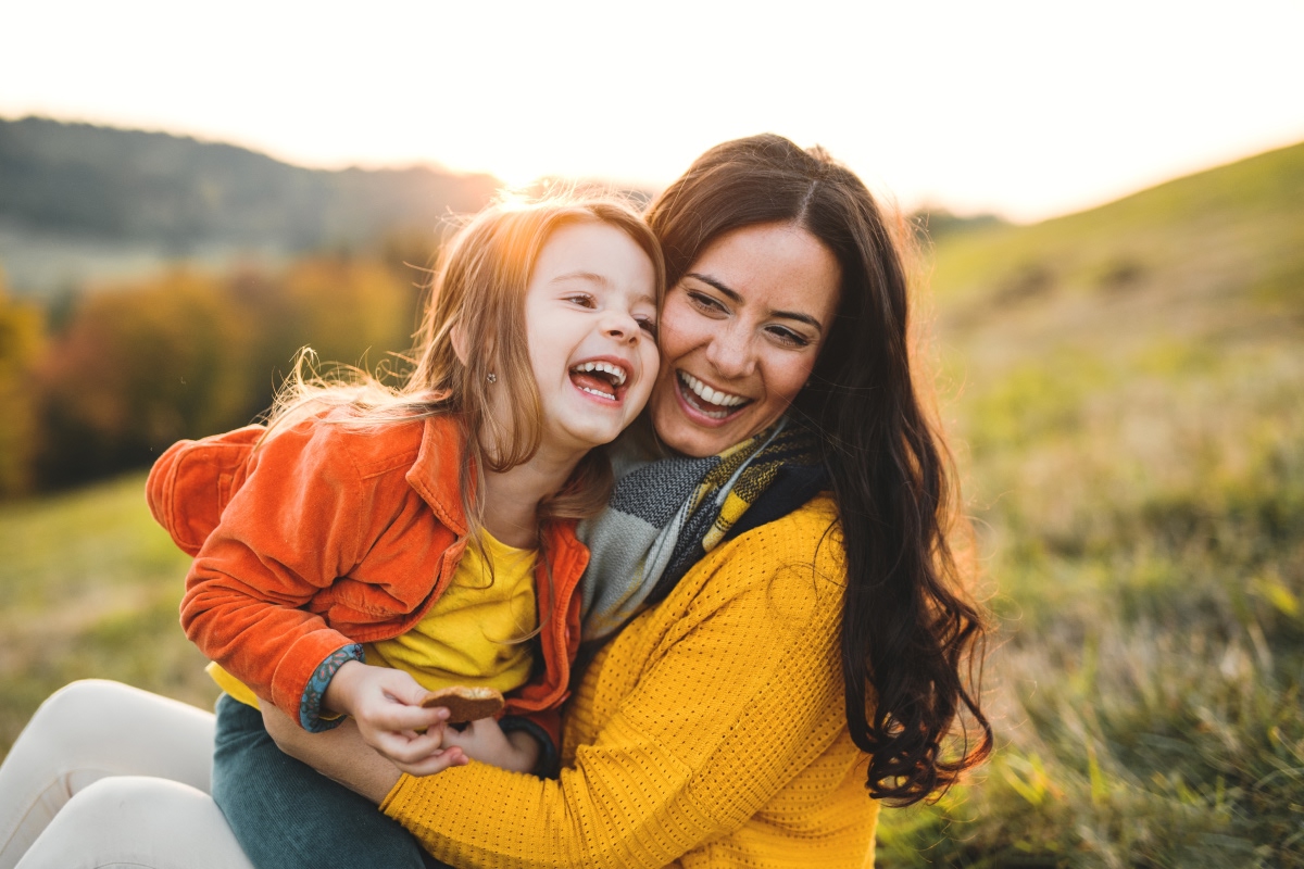 Child sitting on woman’s lap smiling on a hill.
