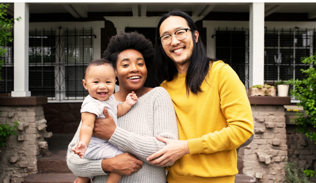 Un homme et une femme tenant leur bébé qui sourient en regardant directement l’objectif.