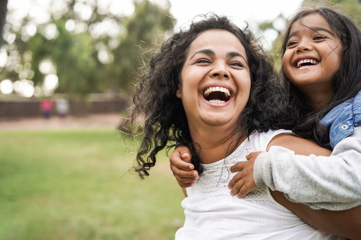 Une petite fille sur le dos d’une femme, toutes deux souriantes.