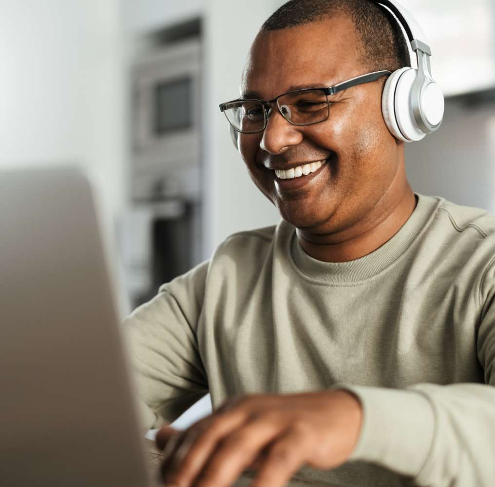 Man smiling while using his laptop and wearing headphones.