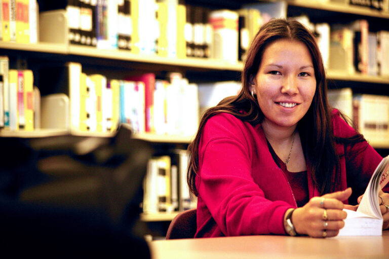 A woman is smiling and looking at the camera with an open book in front of her.